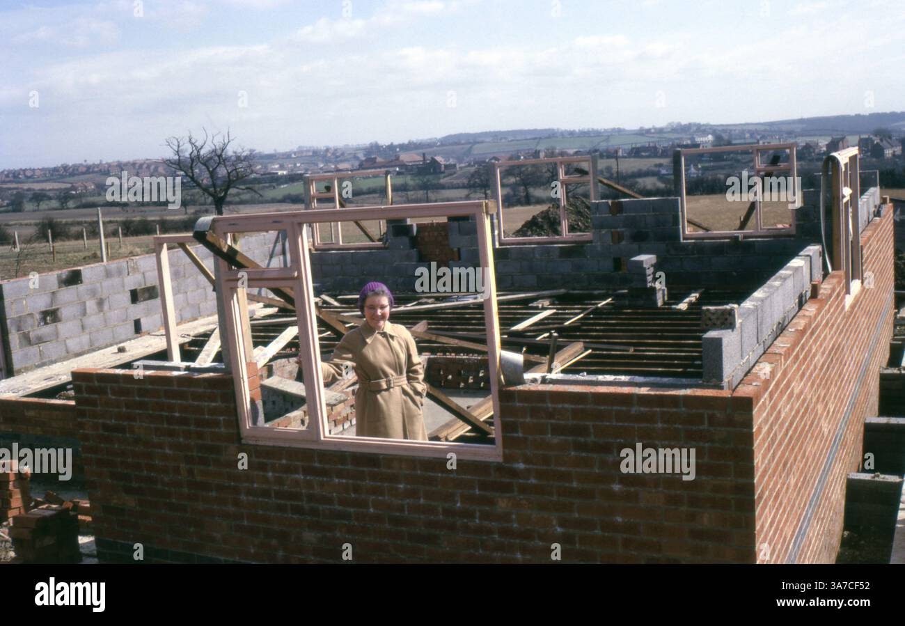 Una donna si trova orgogliosamente nel cantiere della sua futura casa, catturata nel giugno 1965. Circondata da campagna e muratura, l'immagine mostra le prime fasi dell'edificio domestico nel 1960 in Gran Bretagna, tra cui cornici per finestre in legno e putrelle per pavimenti in cemento. Foto Stock