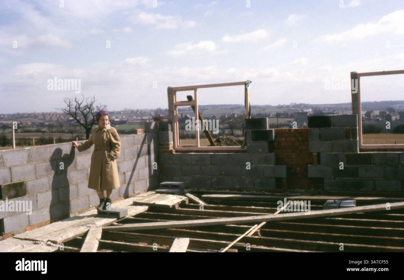 Una donna si trova all'interno delle mura parzialmente costruite della sua futura casa, osservando i progressi della costruzione. Catturata nel giugno 1965 su pellicola da 35 mm, l'immagine offre uno sguardo sulle aspirazioni domestiche e sullo sviluppo abitativo del dopoguerra nella Gran Bretagna degli anni '1960. Foto Stock