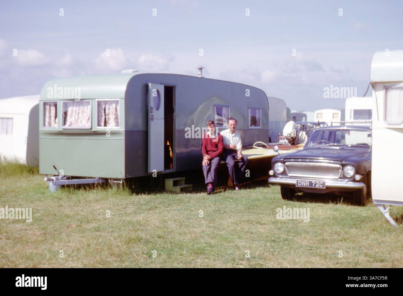 Due uomini si godono una giornata di sole fuori dalla propria roulotte in un parco vacanze britannico, con una classica Ford Zephyr parcheggiata nelle vicinanze. Scattata nel settembre 1966, questa immagine cattura un'istantanea del tempo libero della metà del XX secolo nel Regno Unito, mostrando la cultura della carovaniera d'epoca e l'automobilismo degli anni '1960. Foto Stock