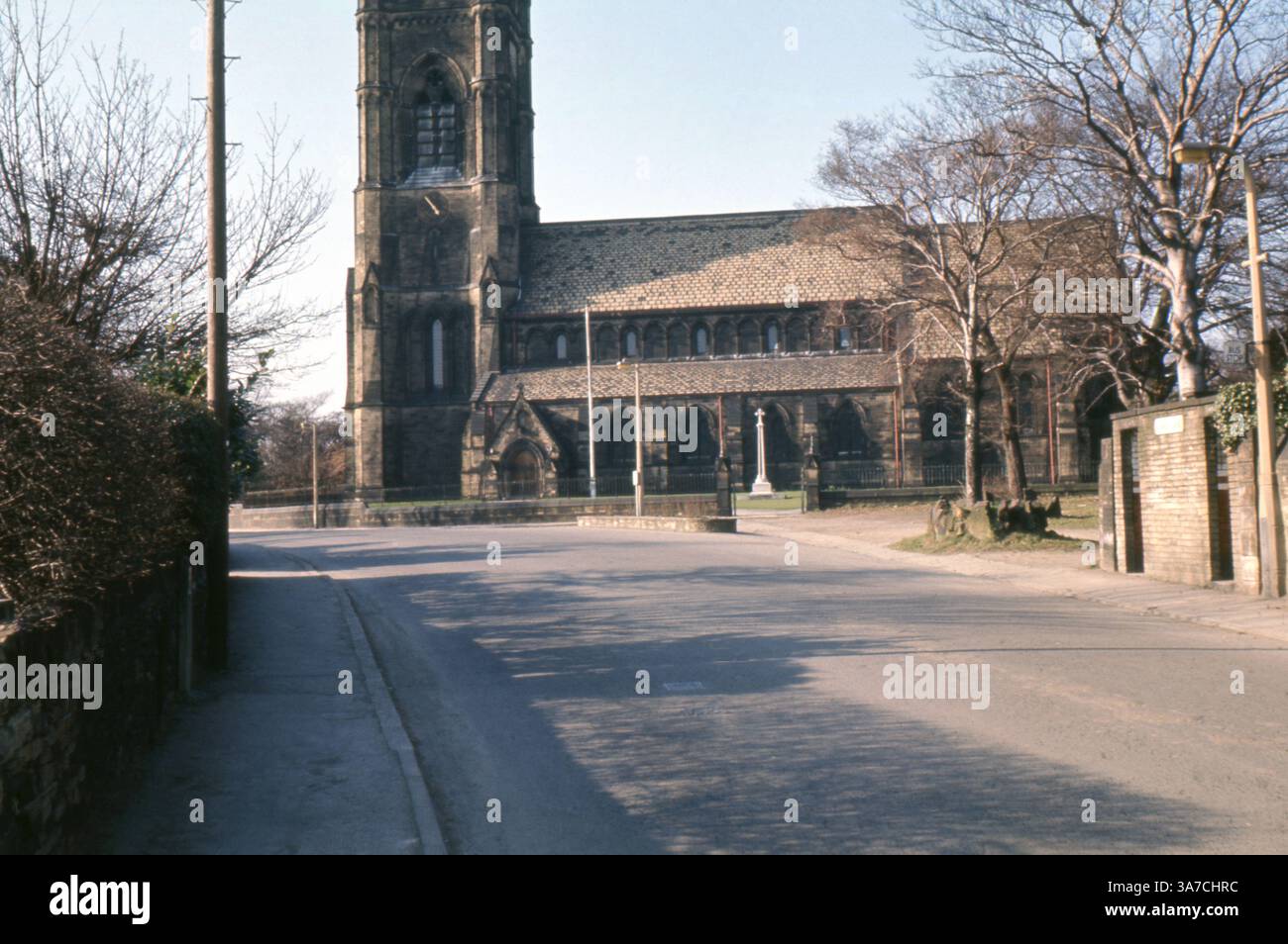 Una veduta di Dewsbury Minster nel West Yorkshire, catturata nell'aprile 1969. La chiesa storica si erge in modo prominente alla luce del sole primaverile, con la sua architettura in stile gotico e la torre centrale visibile dalla tranquilla strada suburbana. Foto Stock