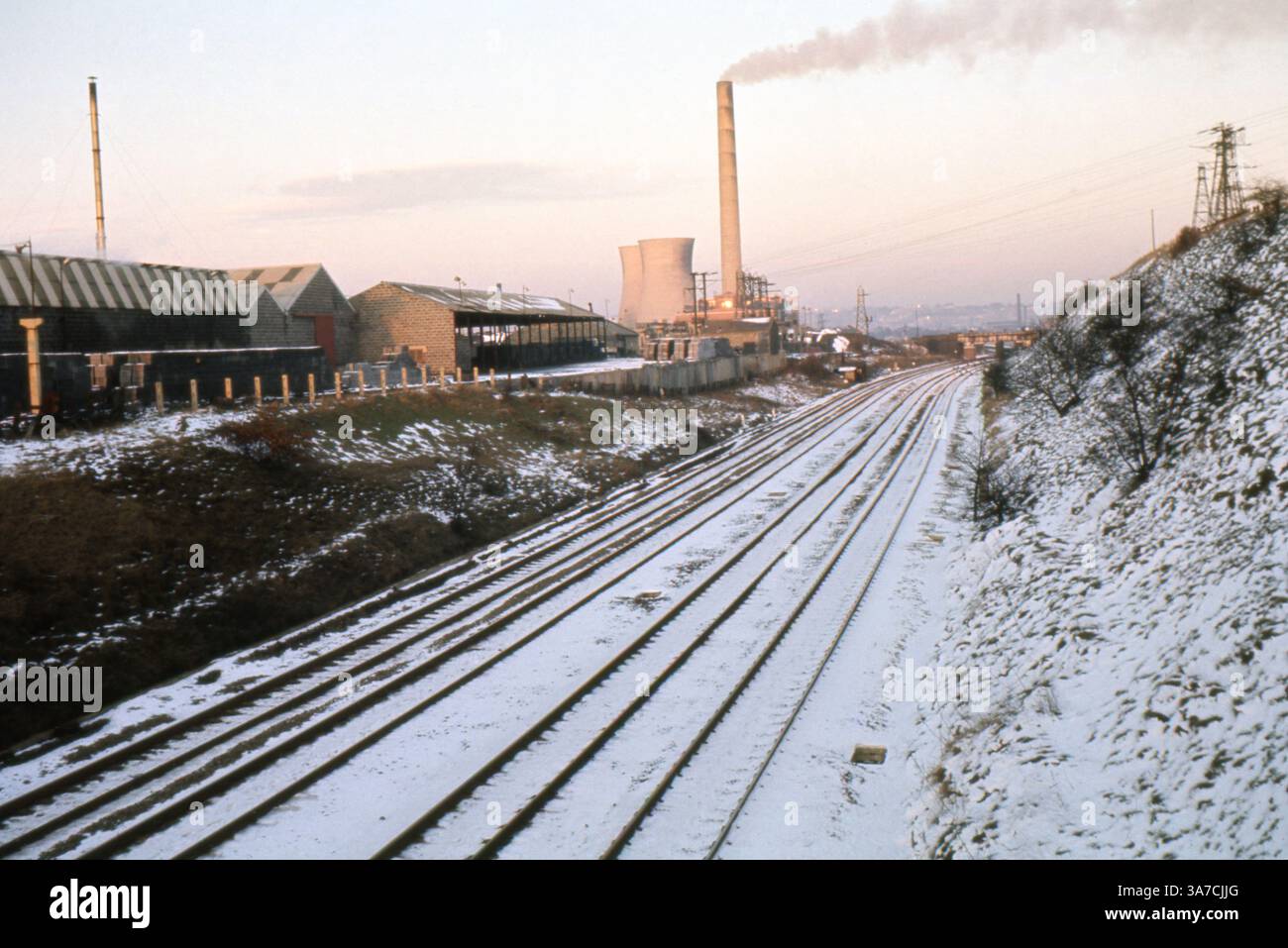 Questa foto originale da 35 mm di aprile 1969 cattura la centrale elettrica Thornhill a Dewsbury, West Yorkshire, in una giornata di neve. L'immagine mostra diversi binari ferroviari innevati che conducono al complesso industriale, con le sue alte camini che emettono fumo e torri di raffreddamento in vista. Il primo piano comprende edifici industriali e capannoni, che illustrano il carattere industriale dell'Inghilterra settentrionale durante questo periodo. Foto Stock
