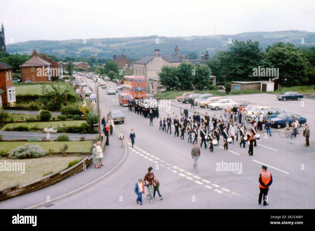 Una vivace parata del giorno di maggio a Mirfield, West Yorkshire, durante gli anni '1970 La sfilata si sposta lungo Dunbottle Lane, con bande in uniforme, striscioni e folle di spettatori che fiancheggiano la strada Foto Stock