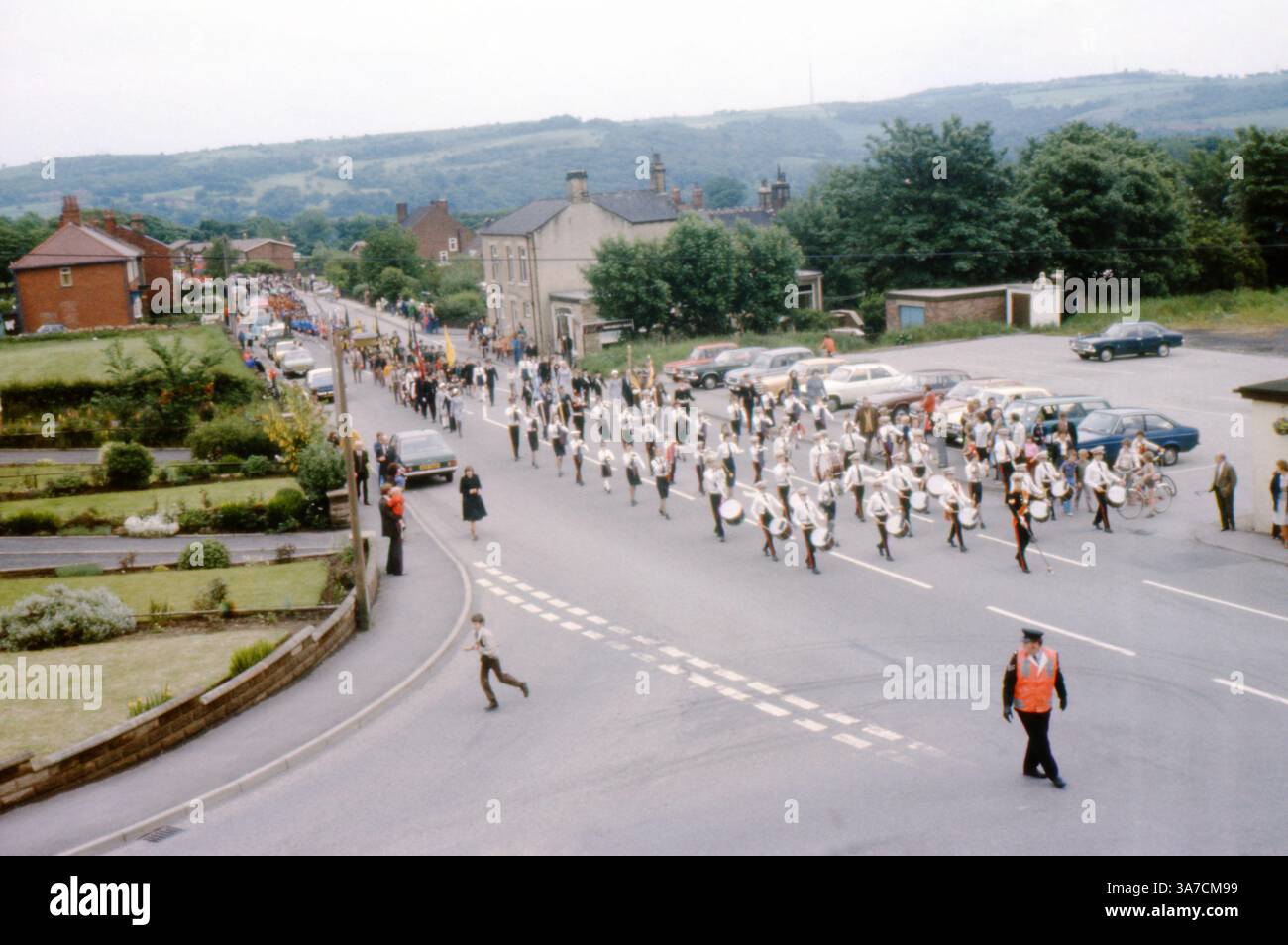 Una vivace parata del giorno di maggio a Mirfield, West Yorkshire, durante gli anni '1970 La sfilata si sposta lungo Dunbottle Lane, con bande in uniforme, striscioni e folle di spettatori che fiancheggiano la strada Foto Stock