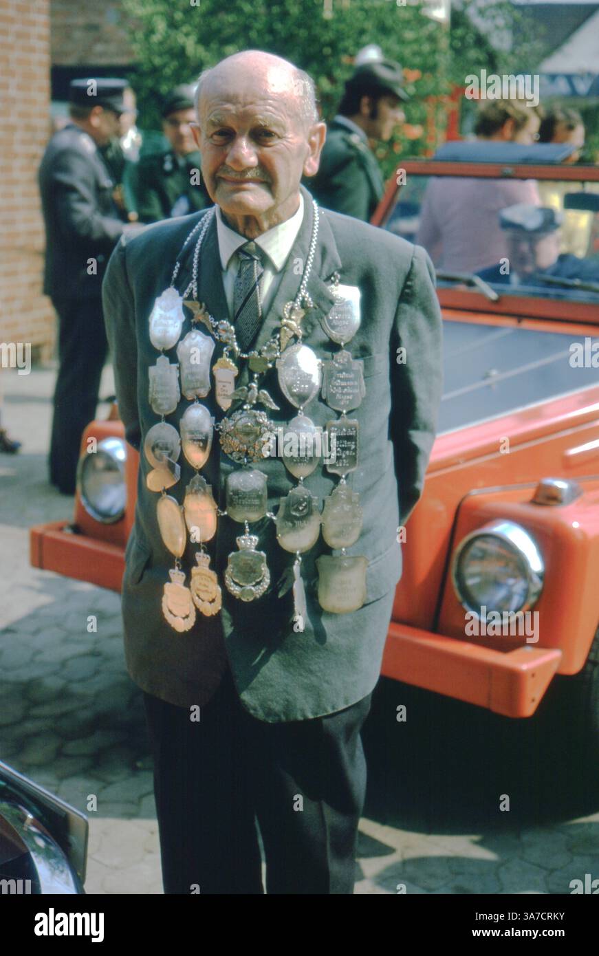 Un membro anziano della Schützen-Gesellschaft di Aligse, Germania, espone con orgoglio una catena cerimoniale di targhe e distinzioni d'argento al 1974 Schützenfest. Il suo ruolo distinto e le sue estese decorazioni suggeriscono uno status di fondazione o onorario all'interno della società dei tiratori locali. Foto Stock