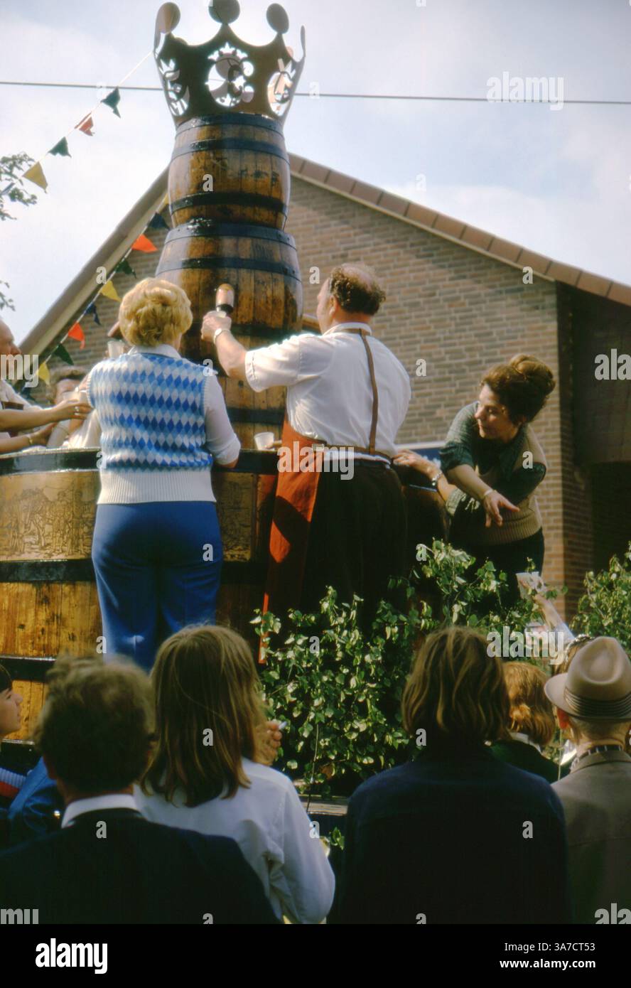 I partecipanti al festival si affollano intorno a un'imponente botte di birra in legno con la corona al 1974 Schützenfest di Aligse, Germania. Le persone riempiono le tazze dai rubinetti come parte di un galleggiante celebrativo sponsorizzato da Einbecker Bier, che simboleggia la tradizione, la comunità e lo spirito festivo in questo vivace raduno rurale. Foto Stock