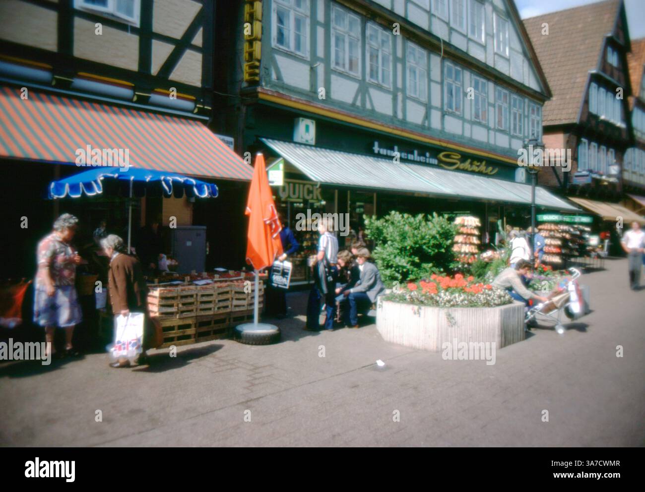 Scena di strada a celle, Germania, luglio 1979. La gente del posto fa shopping e si rilassa nel centro della città tra edifici in legno. Sotto le tende a strisce sono visibili una bancarella di frutta e un negozio di scarpe, mentre la gente si riunisce vicino ai fioristi in una vivace zona pedonale. Foto Stock