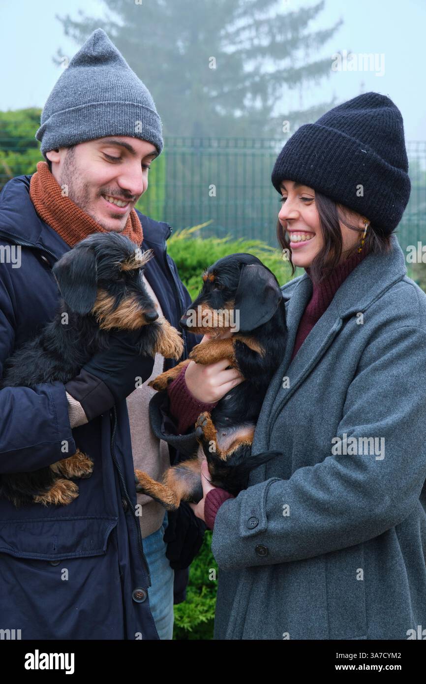 Giovane coppia che tiene in mano le loro due adorabili distese, sorridendo e godendo una giornata nebbiosa nella natura Foto Stock