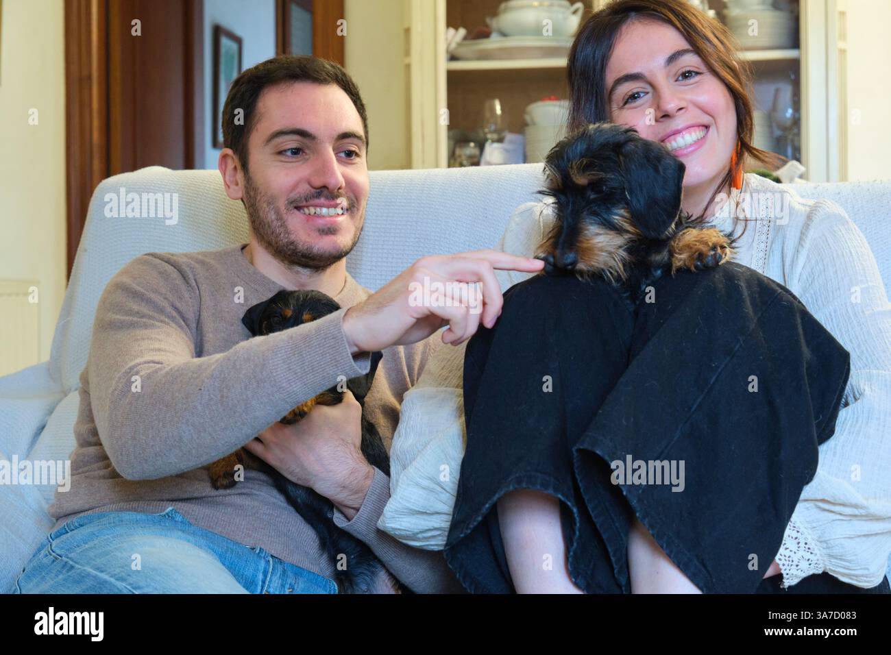 Coppia felice che si rilassa sul divano con due cuccioli: Mostrando affetto e divertendosi insieme Foto Stock