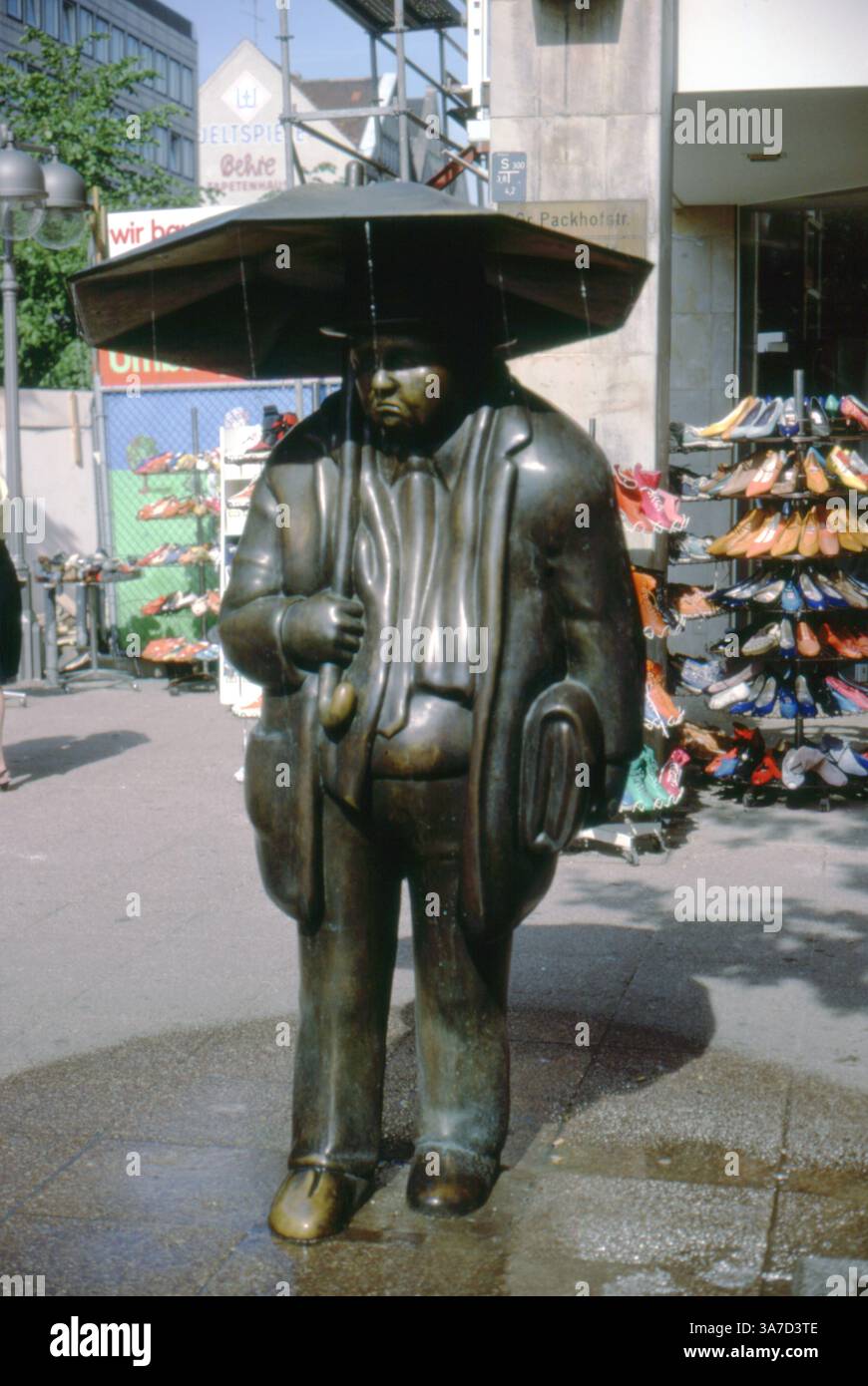 Fotografata nell'agosto 1986 ad Hannover, Germania, questa stravagante scultura in bronzo intitolata Der Reisende (il viaggiatore) si trova all'angolo di Packhofstraße. Creata dallo scultore tedesco Karl-Henning Seemann, la figura di un pendolare stanco con una valigia e un ombrello funziona anche come una fontana, con l'acqua che scorre dai bordi dell'ombrello. Foto Stock