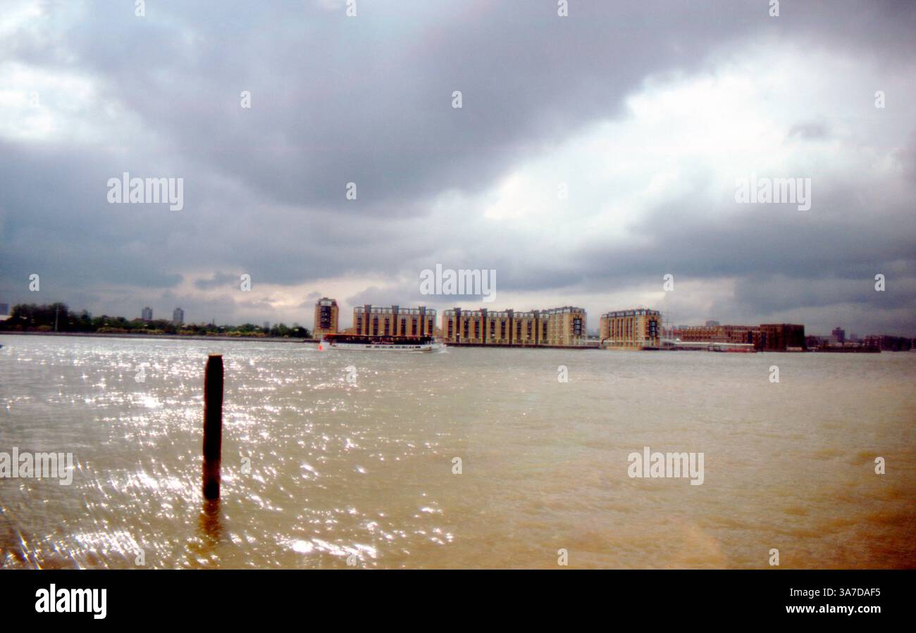 Vista sul Tamigi verso Rotherhithe, Londra, con Lawrence Wharf e gli sviluppi dell'Old Nelson Dock sotto cieli spettacolari nel giugno 1991. Un battello fluviale passa di fronte ai magazzini sul fiume recentemente convertiti. Foto Stock