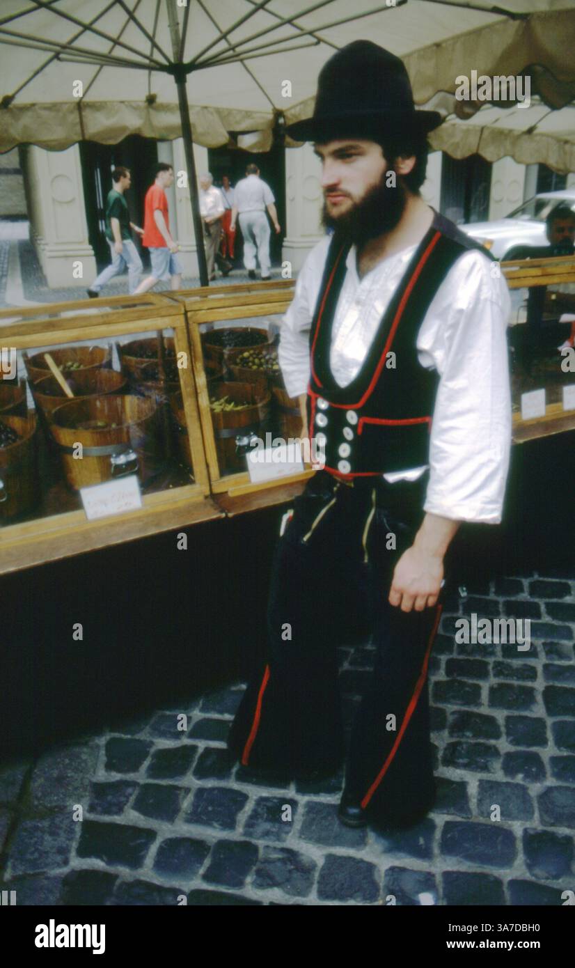 Un giovane in costume tradizionale tedesco da viaggio (Geselle) si trova in una bancarella del mercato, probabilmente durante una festa culturale o commerciale a Hildesheim, in Germania. Il suo vestito, tra cui un cappello a tesa larga, gilet con bottoni e pantaloni svasati, rappresenta la tradizione secolare dei commercianti che viaggiano durante il loro apprendistato. Foto Stock