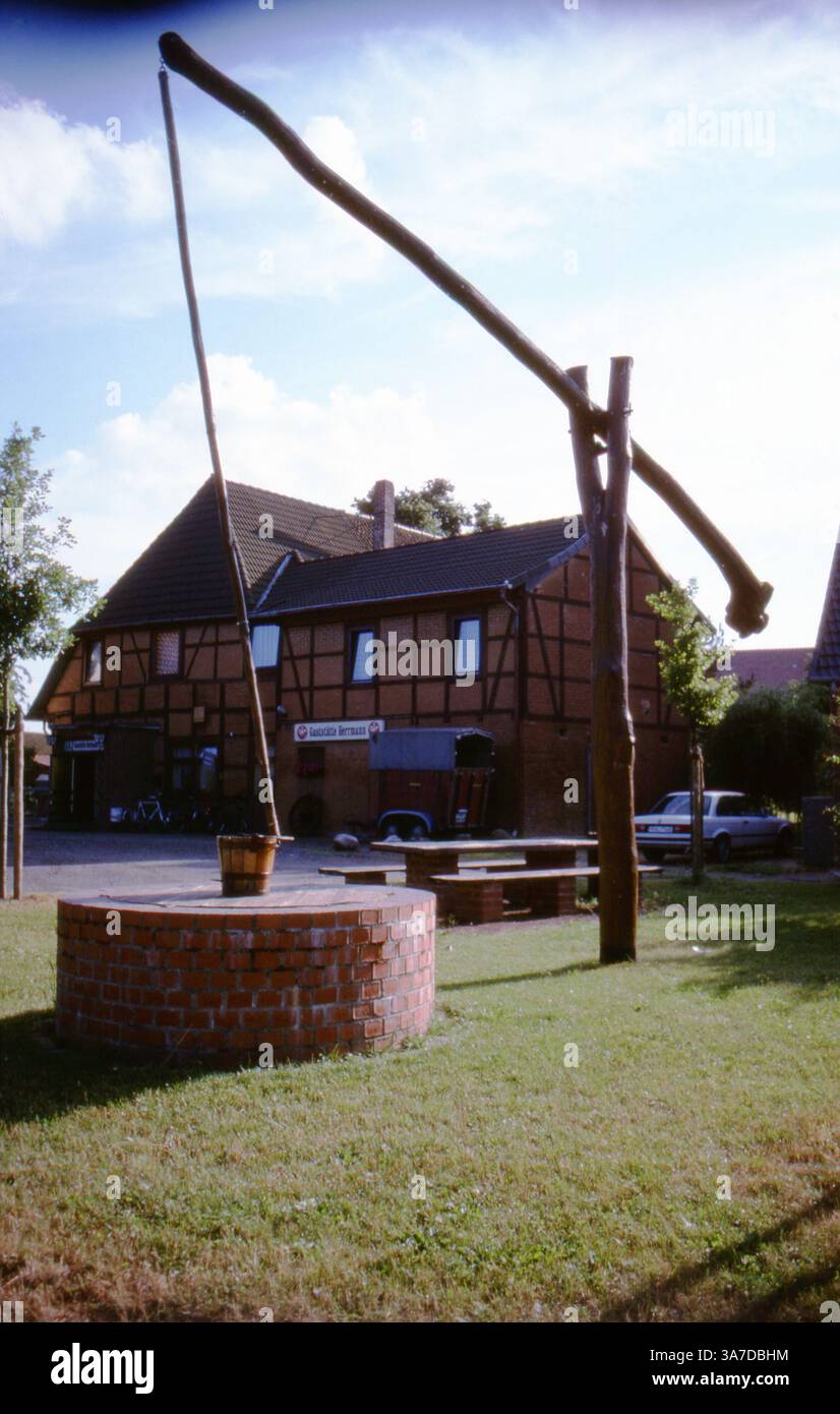 Un antico pozzo di legno con un palo (noto come "Schwengelbrunnen") a Sievershausen, Germania. Dietro di essa si trova una tradizionale pensione a graticcio. Ripresa nell'agosto 1992 su pellicola slide da 35 mm. Foto Stock