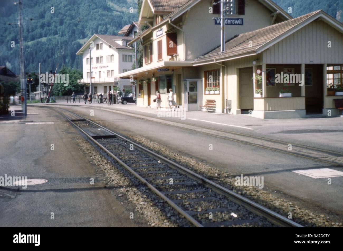 Stazione ferroviaria di Widerswil in Svizzera, fotografata nei primi anni '1960 Adagiata su uno sfondo mozzafiato di paesaggi alpini, la stazione funge da porta d'accesso alla ferrovia Schynige Platte, un percorso popolare per i visitatori che esplorano la regione dell'Oberland Bernese. Foto Stock