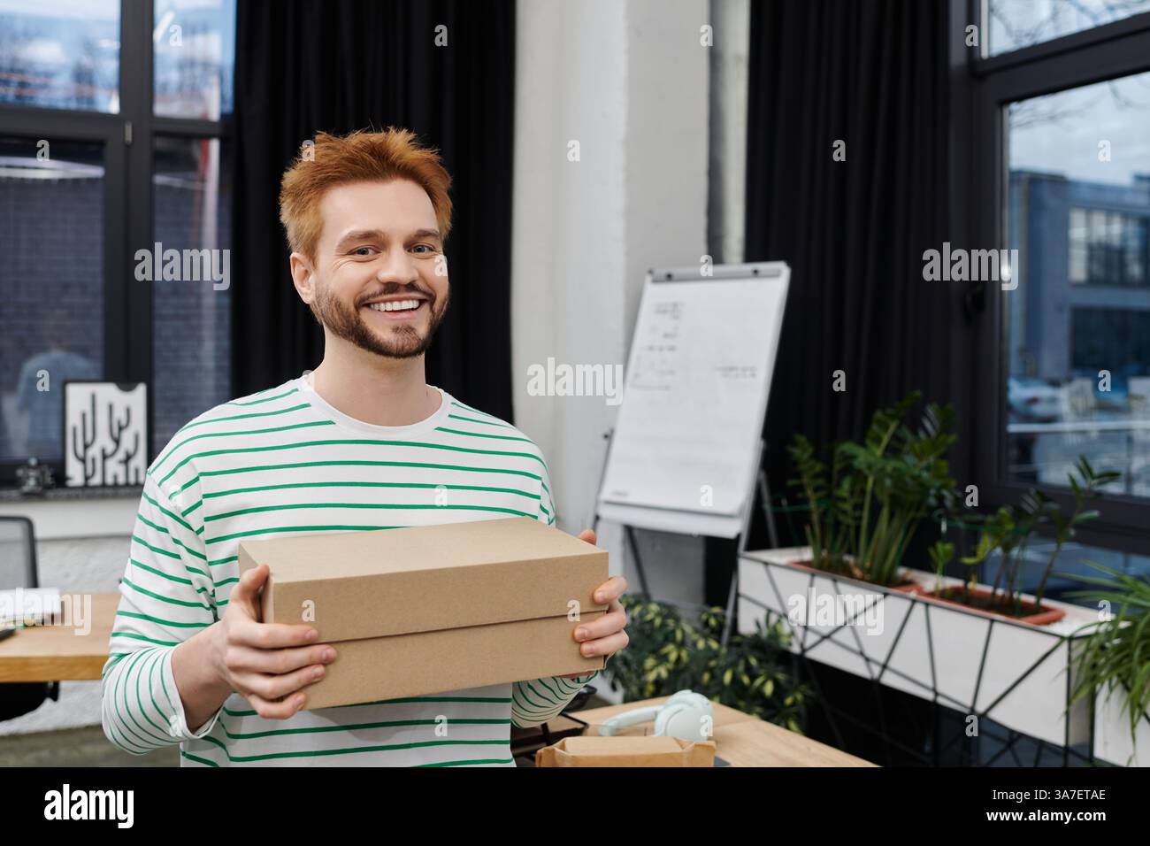 l'uomo sorride mentre tiene in mano una scatola piena, circondata da uno spazio in movimento organizzato e contemporaneo. Foto Stock