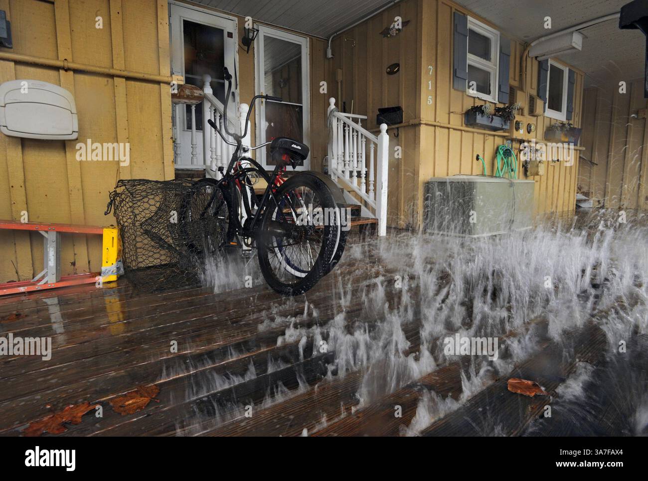 28 ottobre 2012 - Ocean City, Maryland, Stati Uniti - l'impatto degli effetti della tempesta dall'uragano Sandy, che non è ancora arrivato nella regione, crea onde che colpiscono la pancia del ponte che schizza tra le tavole, spruzzando biciclette per bambini che riposano alla porta d'ingresso di un appartamento su Edgewater Avenue a Ocean City domenica. (Immagine di credito: © Karl Merton Ferron/MCT/ZUMAPRESS.com) Foto Stock