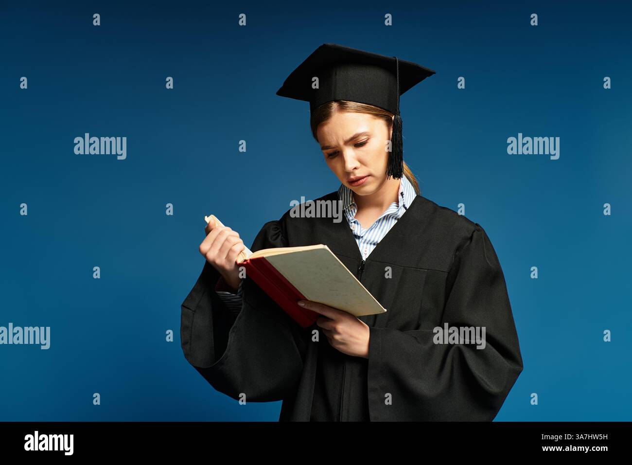 Una giovane donna in abito da laurea, profondamente concentrata su un libro, simboleggia il successo accademico. Foto Stock