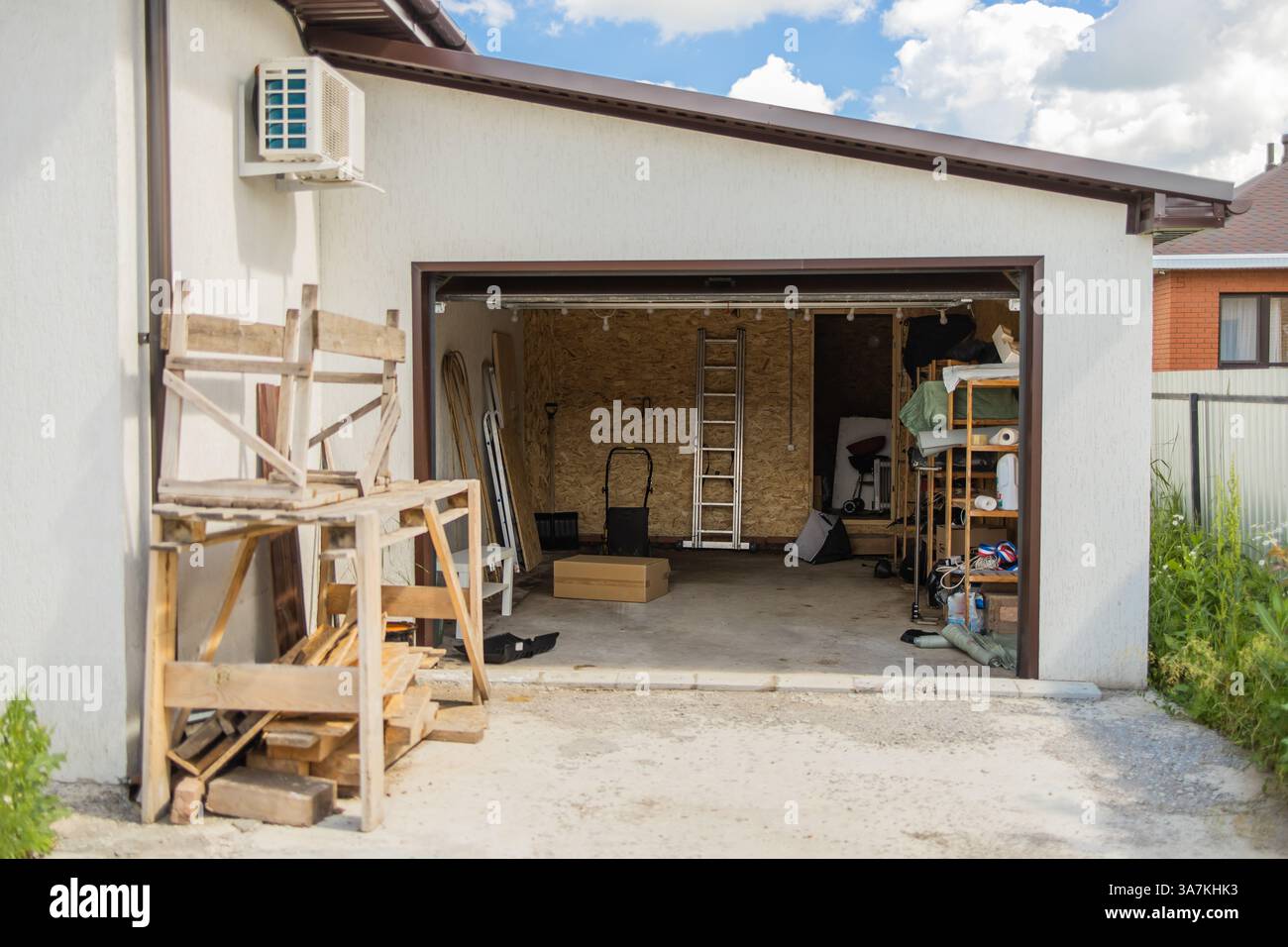 Garage aperto con attrezzi e tavole di legno. Stoccaggio organizzato e uso efficiente dello spazio di lavoro residenziale per la manutenzione domestica. Foto Stock