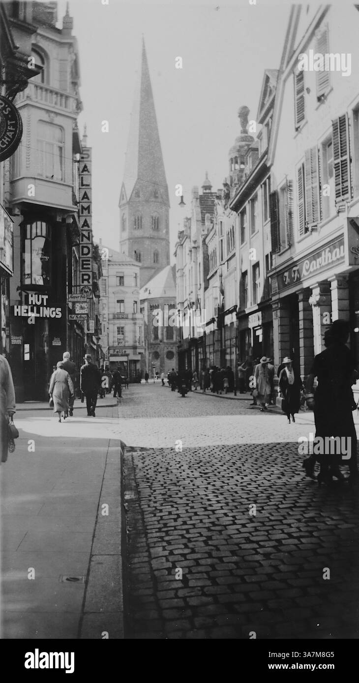1936, scena di strada con affari, pedoni e la torre del Münsterkirche, nota anche come la cattedrale di Bonn, una chiesa romanica con una ricca storia risalente all'XI secolo. Nel 1936, era un importante punto di riferimento a Bonn, servendo come luogo di culto e sito storico. Da una raccolta di fotografie amatoriali non attribuite nell'intervallo di date, 1929-1936, che includono le festività del Regno Unito e dell'Europa. La maggior parte delle immagini originali erano circa 3 ½ x 2 pollici. Foto Stock
