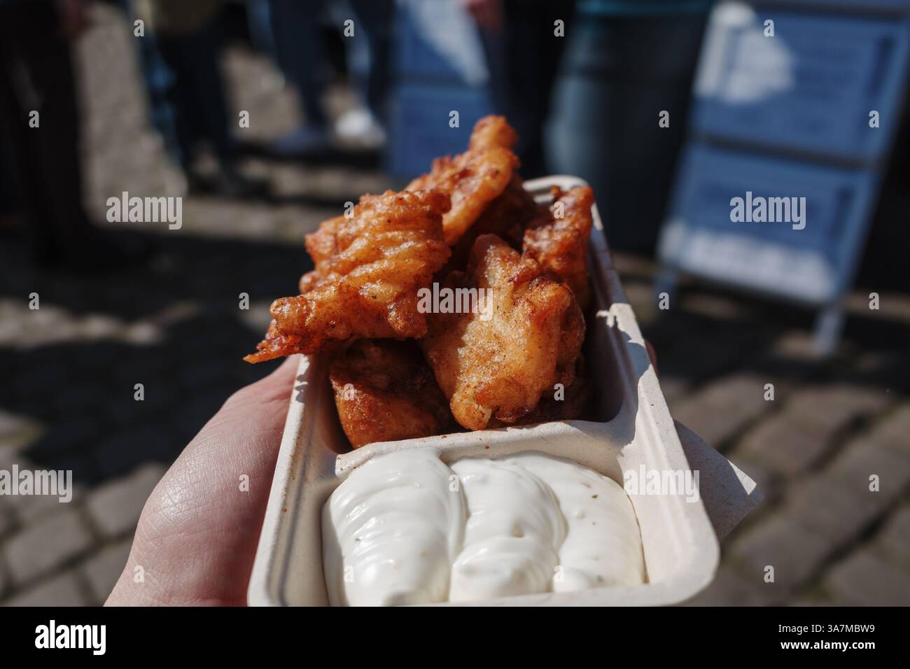 Una vista ravvicinata dei morsi di pesce fritto dorati serviti in un vassoio di cartone con una generosa porzione di salsa all'aglio. Foto Stock