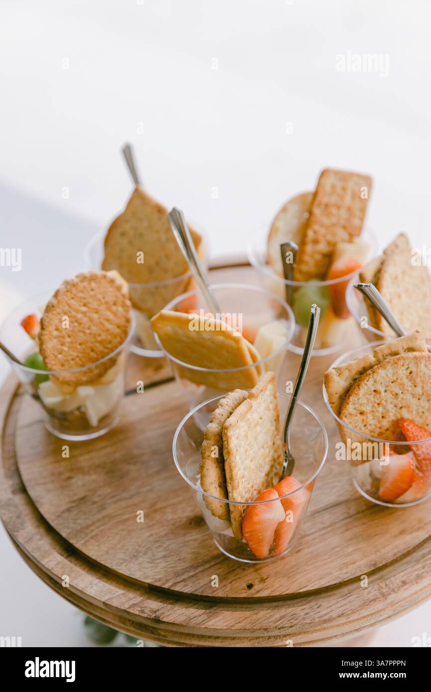 I colorati dessert alla frutta serviti in bicchieri chiari mostrano strati cremosi ricoperti di dolcetti croccanti durante una riunione estiva. Foto Stock