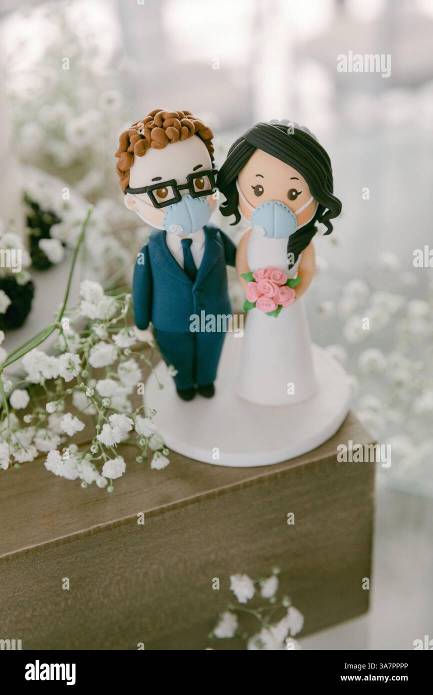 Un unico topper per torta nuziale mostra una coppia che indossa maschere facciali, circondati da delicati fiori, che celebrano l'amore in modo sicuro. Foto Stock