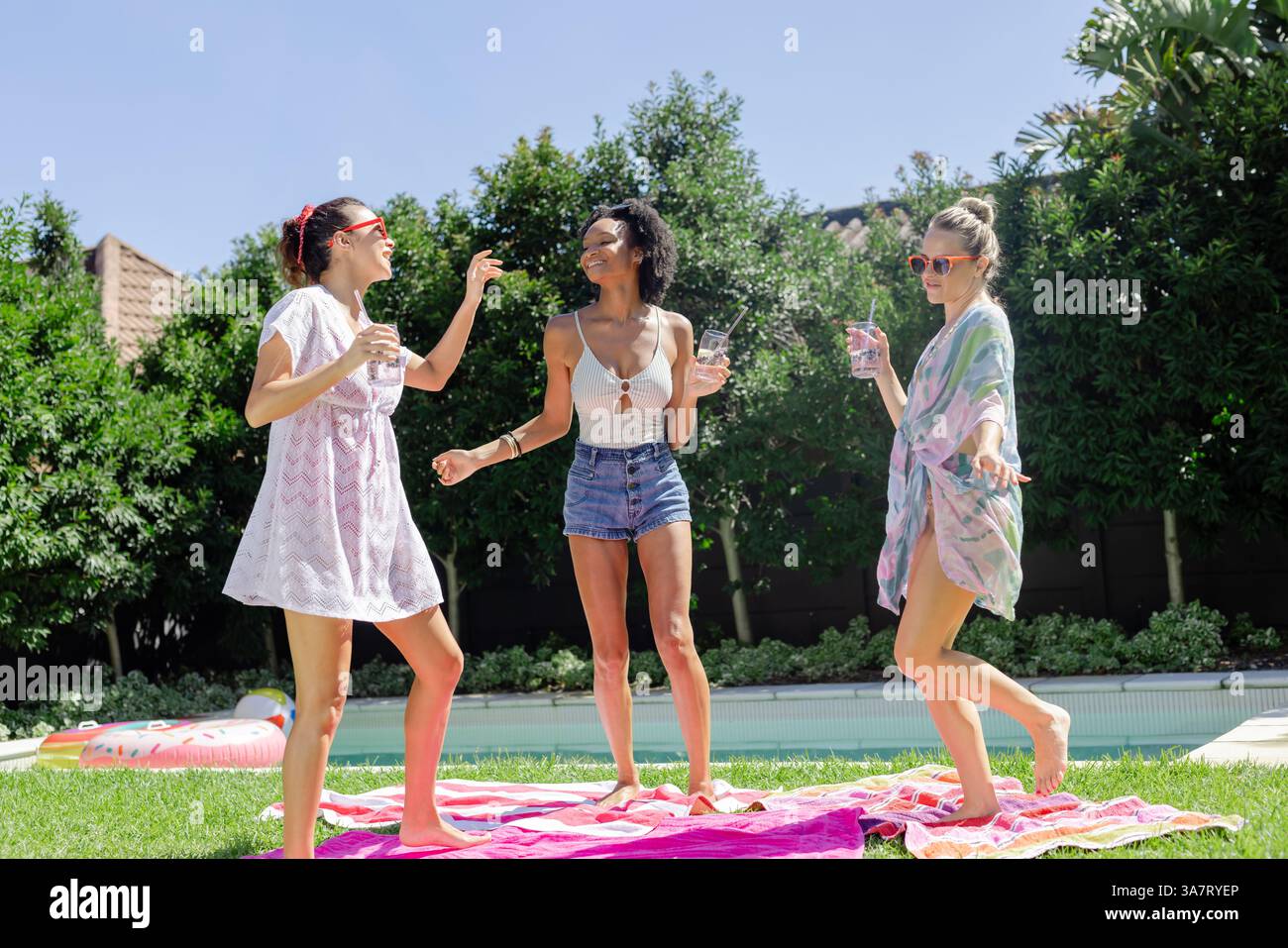 Diverse amiche che ridono e ballano in piscina, godendosi una giornata di sole con bevande e spazio per copiare Foto Stock
