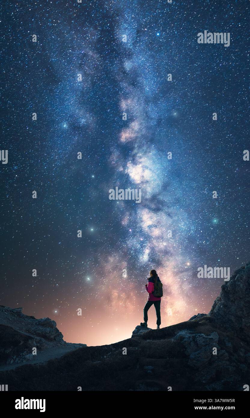 Via Lattea illuminante e donna sulla vetta della montagna nella notte stellata. Dolomiti, Italia. Galassia. Paesaggio spaziale con silhouette di una ragazza, rocce, cielo con bri Foto Stock
