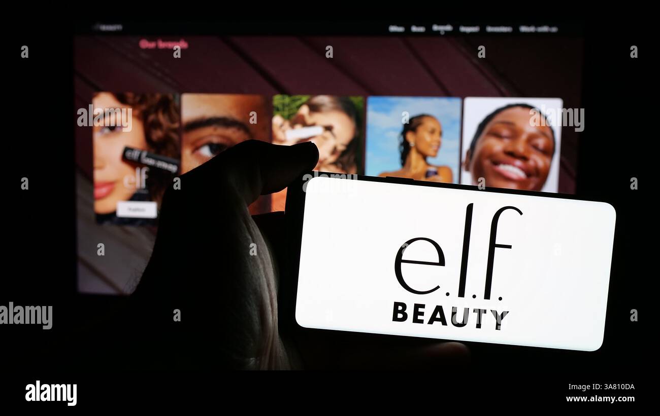 In questa illustrazione fotografica, una persona ha un telefono cellulare con il logo della società di cosmetici americana E.l.f. Beauty Inc. Sullo schermo davanti alla pagina Web. Foto Stock