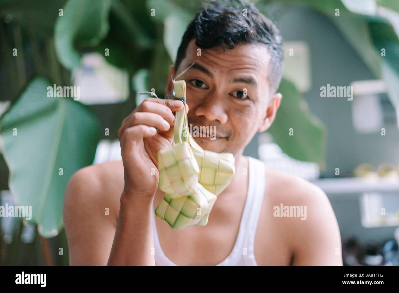 Un uomo regge Ketupat, un tradizionale piatto di riso indonesiano realizzato con foglie di palma intrecciate, durante la celebrazione di Eid al-Fitr. Simboleggia il patrimonio culturale Foto Stock