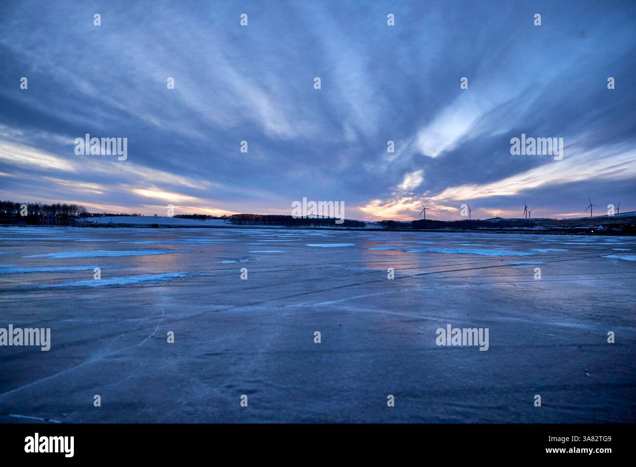 Tramonto invernale su un lago ghiacciato con turbine eoliche Foto Stock