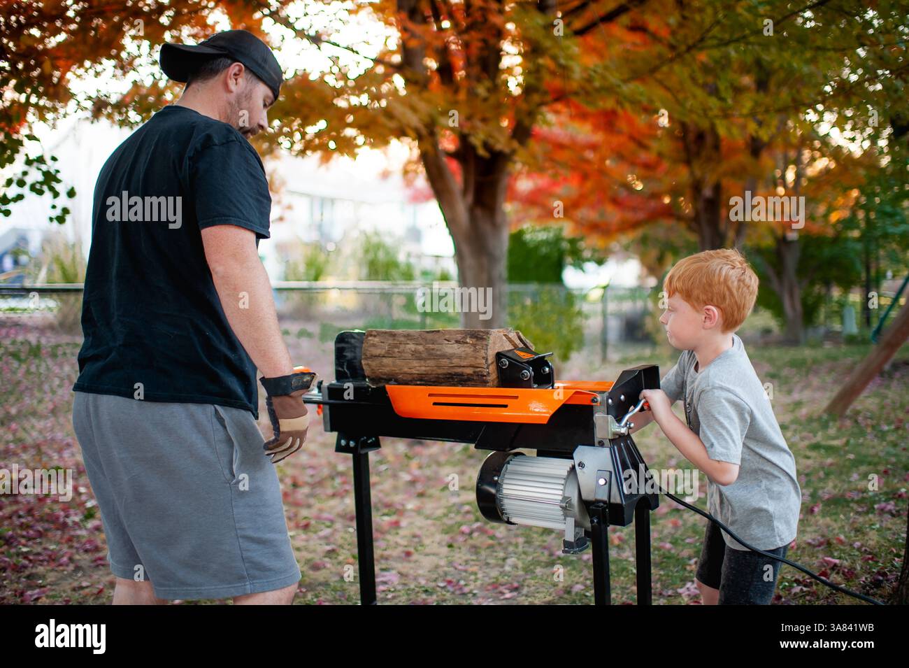 Il ragazzo di 4-5 anni aiuta papà a dividere il legno nel cortile in autunno Foto Stock