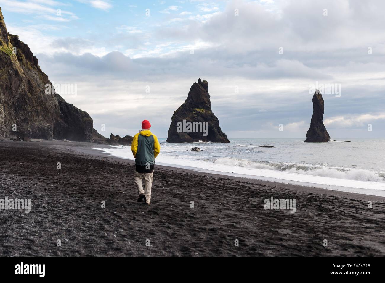 L'uomo osserva potenti onde e faraglioni di mare a Reynisfjara, Vik Foto Stock