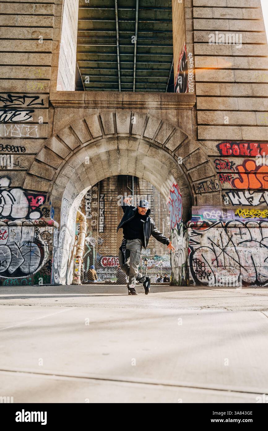 Ballerina di strada in movimento sotto un arco urbano coperto di graffiti Foto Stock