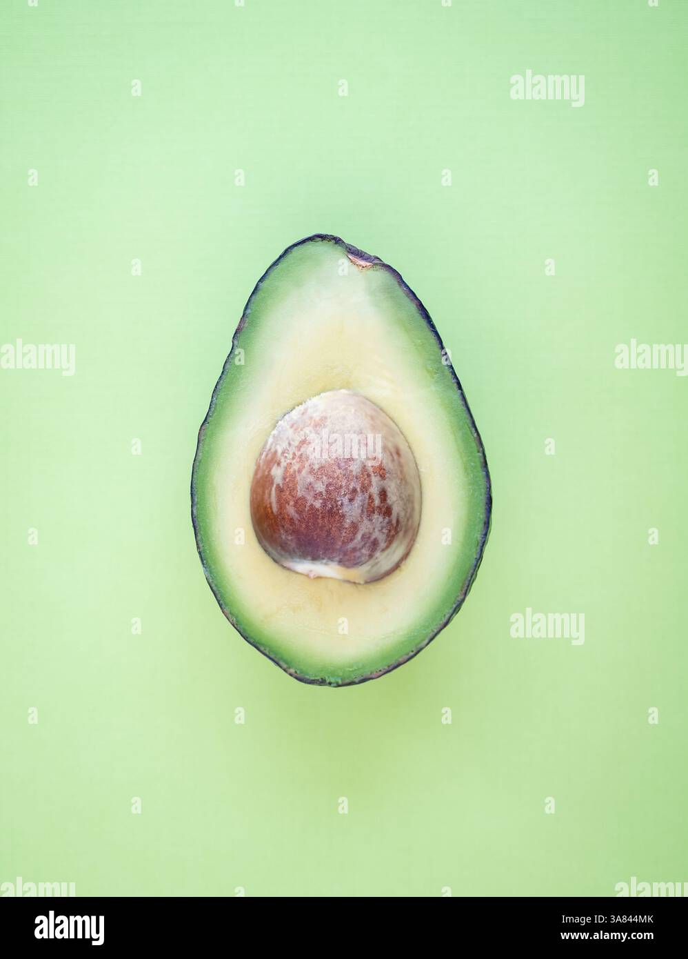 Vista dall'alto del singolo avocado tagliato a metà su sfondo verde pieno. Foto Stock