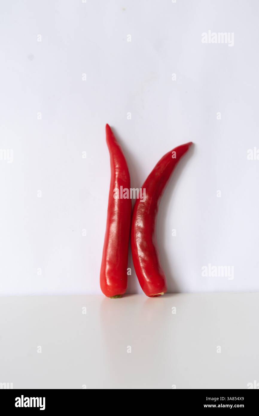 Composizione minimalista con due peperoncini rossi vivaci in posizione verticale su uno sfondo bianco. L'immagine evidenzia la b naturale Foto Stock