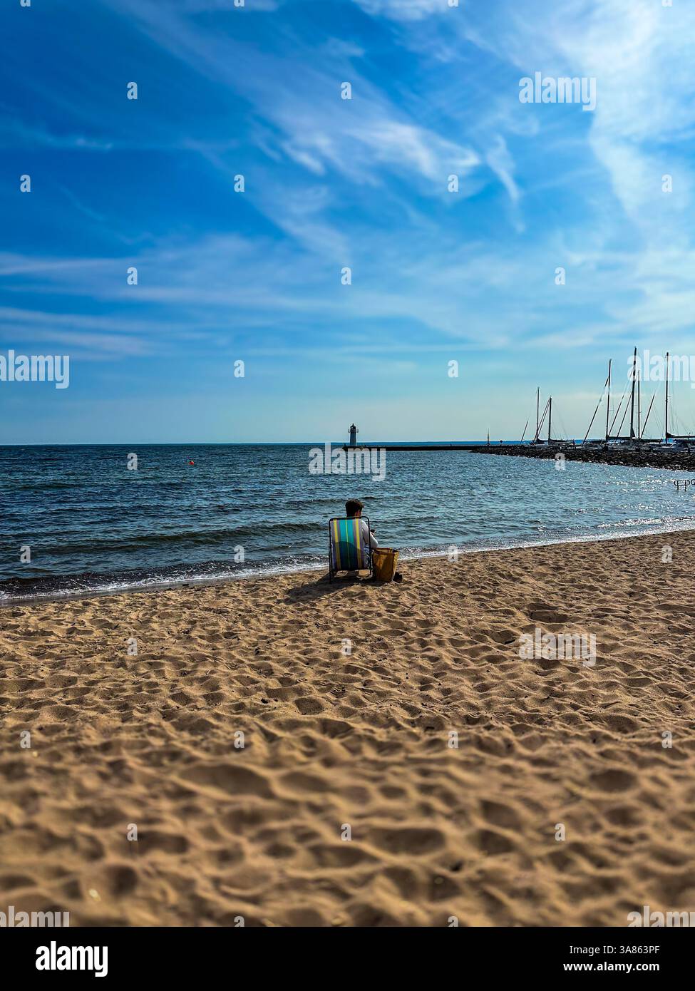 Donna che si rilassa su una sdraio sulla spiaggia con vista sul faro e sul porticciolo in una giornata di sole sul lago Vattern, Svezia. Foto di alta qualità. Foto Stock