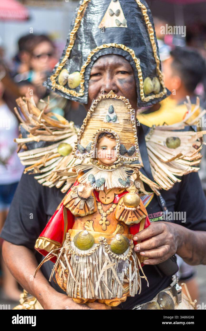 Un partecipante al festival di Atiatihan in costume colorato che tiene un'immagine dello sto Niño durante la celebrazione a Kalibo, nelle Filippine Foto Stock