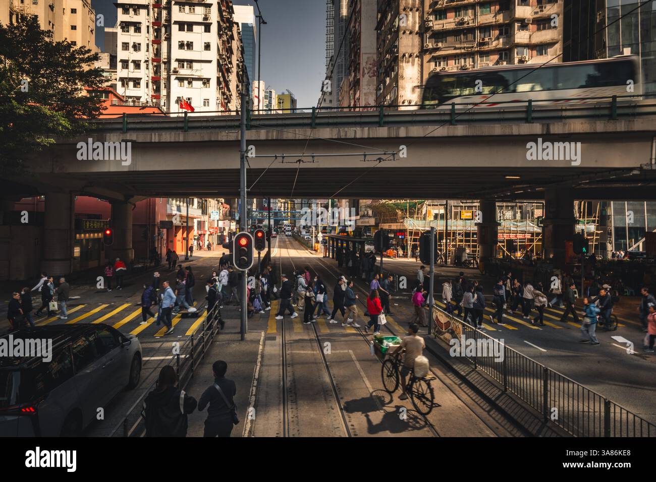 Una scena di strada con un tram di Hong Kong sullo sfondo con pedoni che attraversano una strada trafficata, Hong Kong, Cina Foto Stock