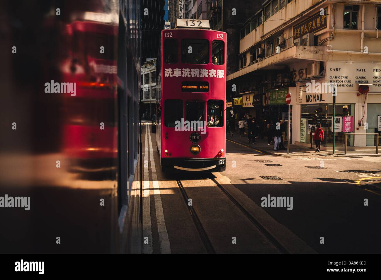 Una fotografia artistica di un tram rosa di Hong Kong che attraversa una striscia di luce solare mentre arriva a Hong Kong, in Cina Foto Stock
