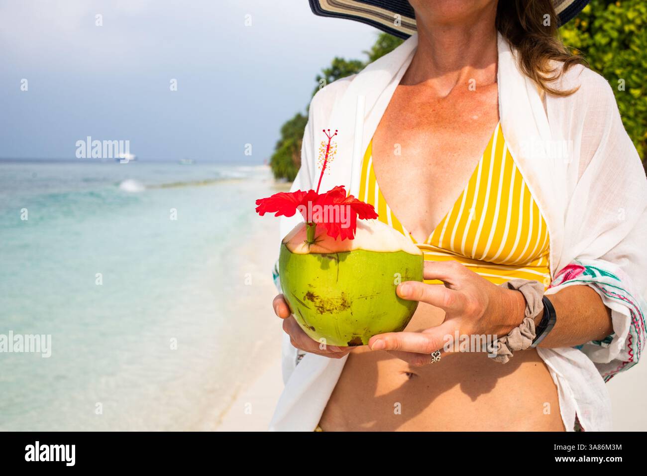 Donna che tiene la noce di cocco sulla spiaggia tropicale, le Maldive, l'Oceano Indiano Foto Stock