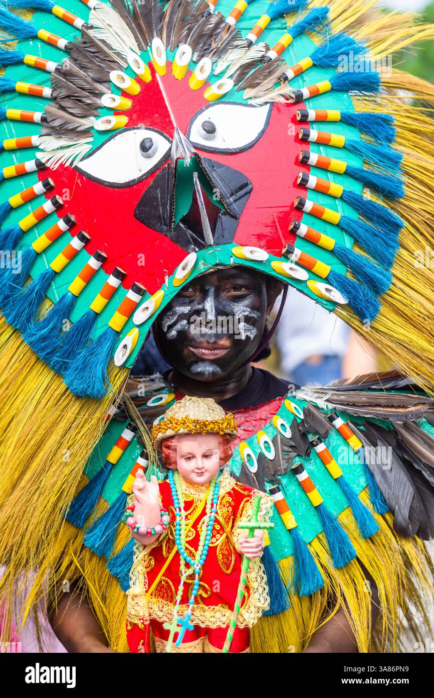 Un partecipante al festival di Atiatihan in costume colorato che tiene un'immagine dello sto Niño durante la celebrazione a Kalibo, nelle Filippine Foto Stock