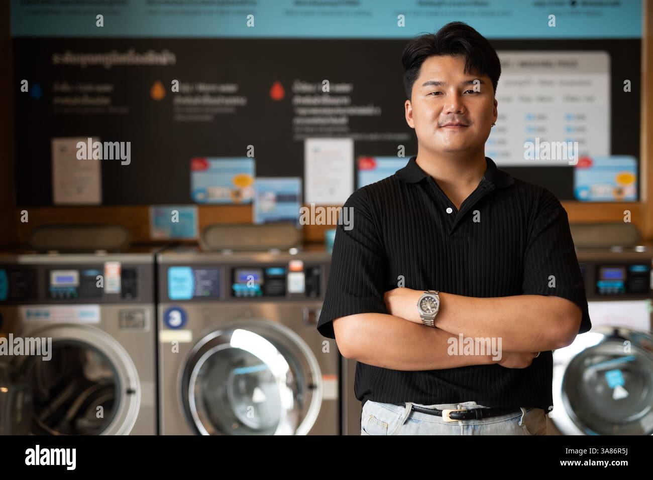 Giovane asiatico in lavanderia con le braccia incrociate Foto Stock