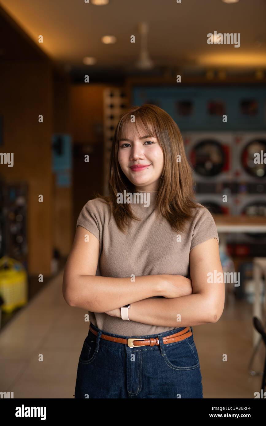 Giovane donna asiatica in negozio di lavanderia con le braccia incrociate Foto Stock
