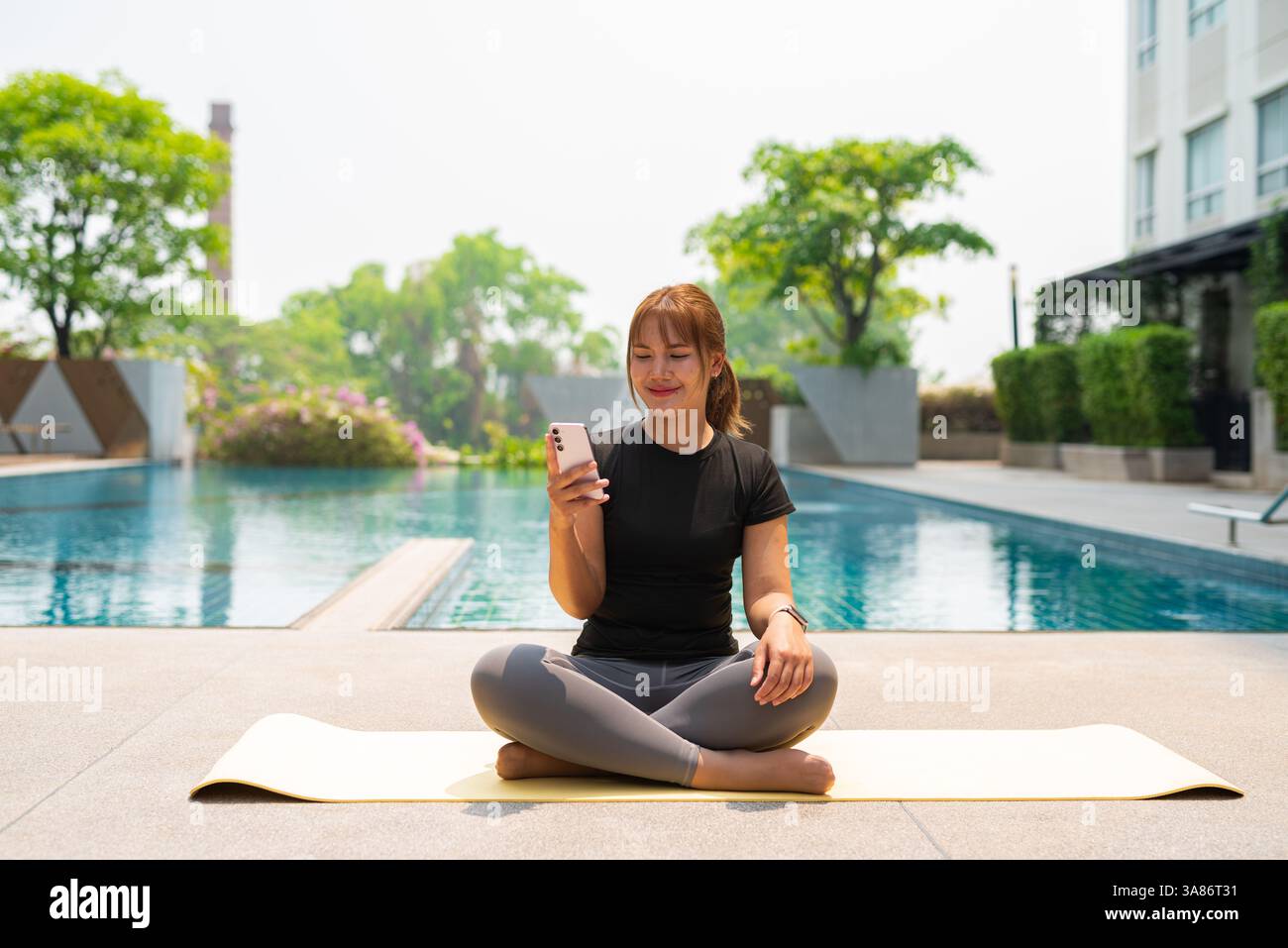 Giovane donna asiatica che fa esercizio di yoga accanto alla piscina durante l'estate Foto Stock