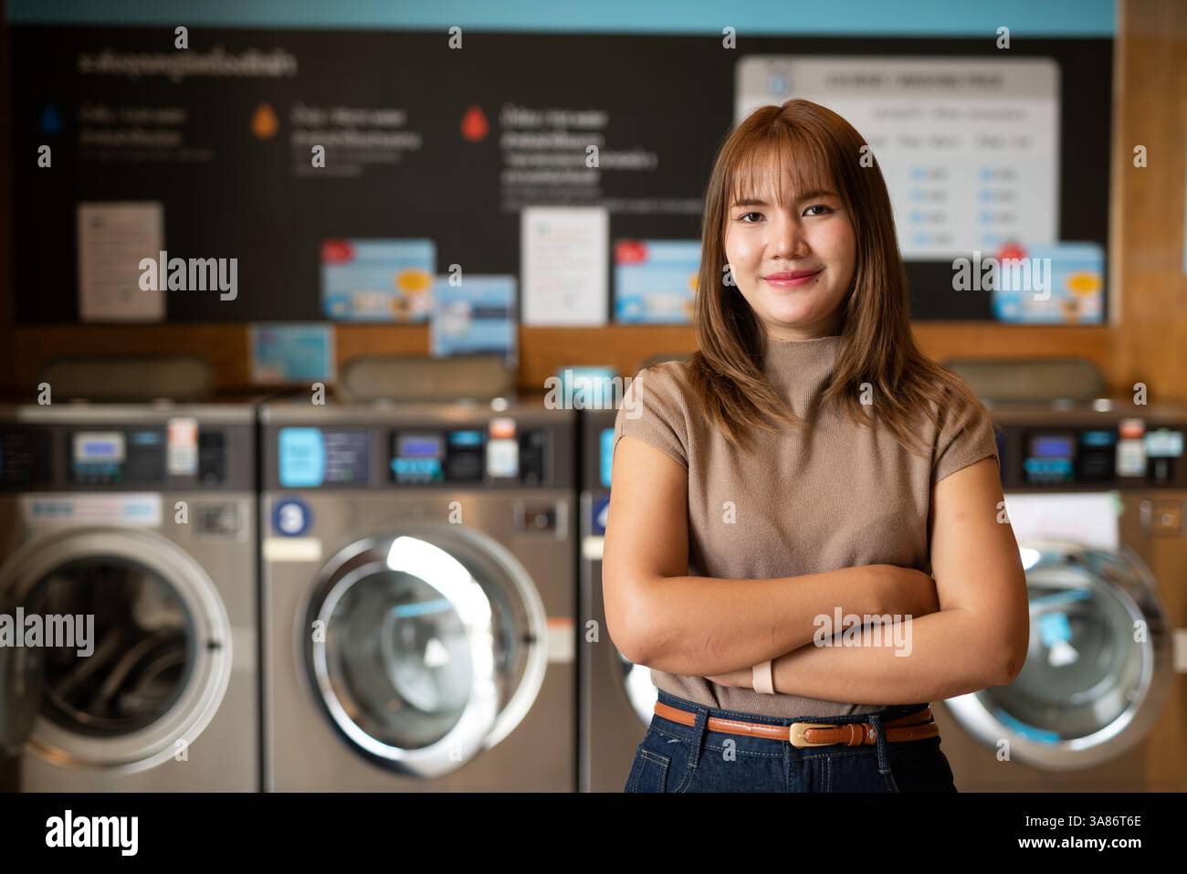 Giovane donna asiatica in negozio di lavanderia con le braccia incrociate Foto Stock