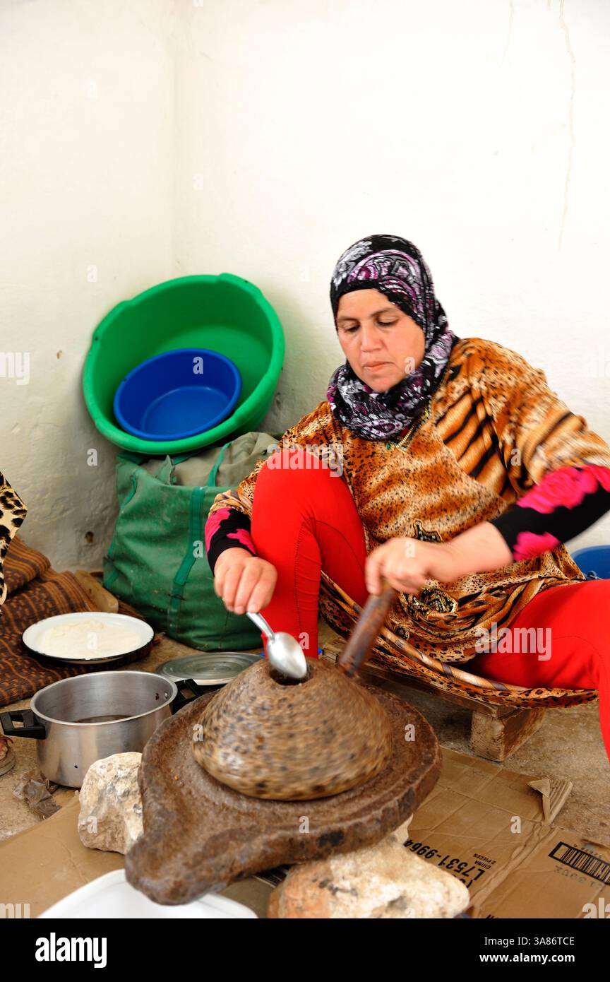 Donna che macina semi di argan per ottenere olio, famiglia Saadia, villaggio Tagante, Anti-Atlas, Marocco Foto Stock