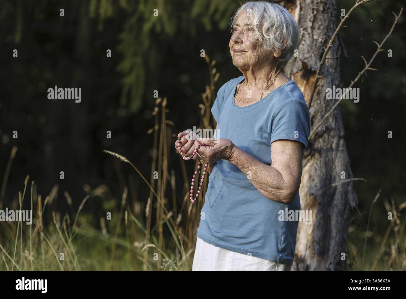 Donna anziana che prega con perline di preghiera in un giardino, Francia Foto Stock