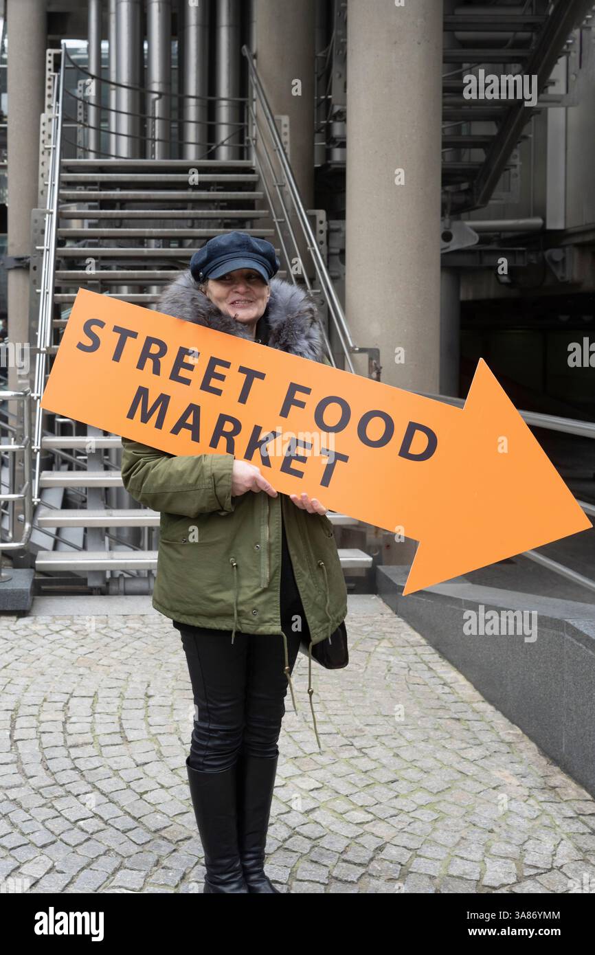 Una donna ha in mano il cartello "Street Food Market", che dirige i passanti, probabilmente nella City di Londra Foto Stock