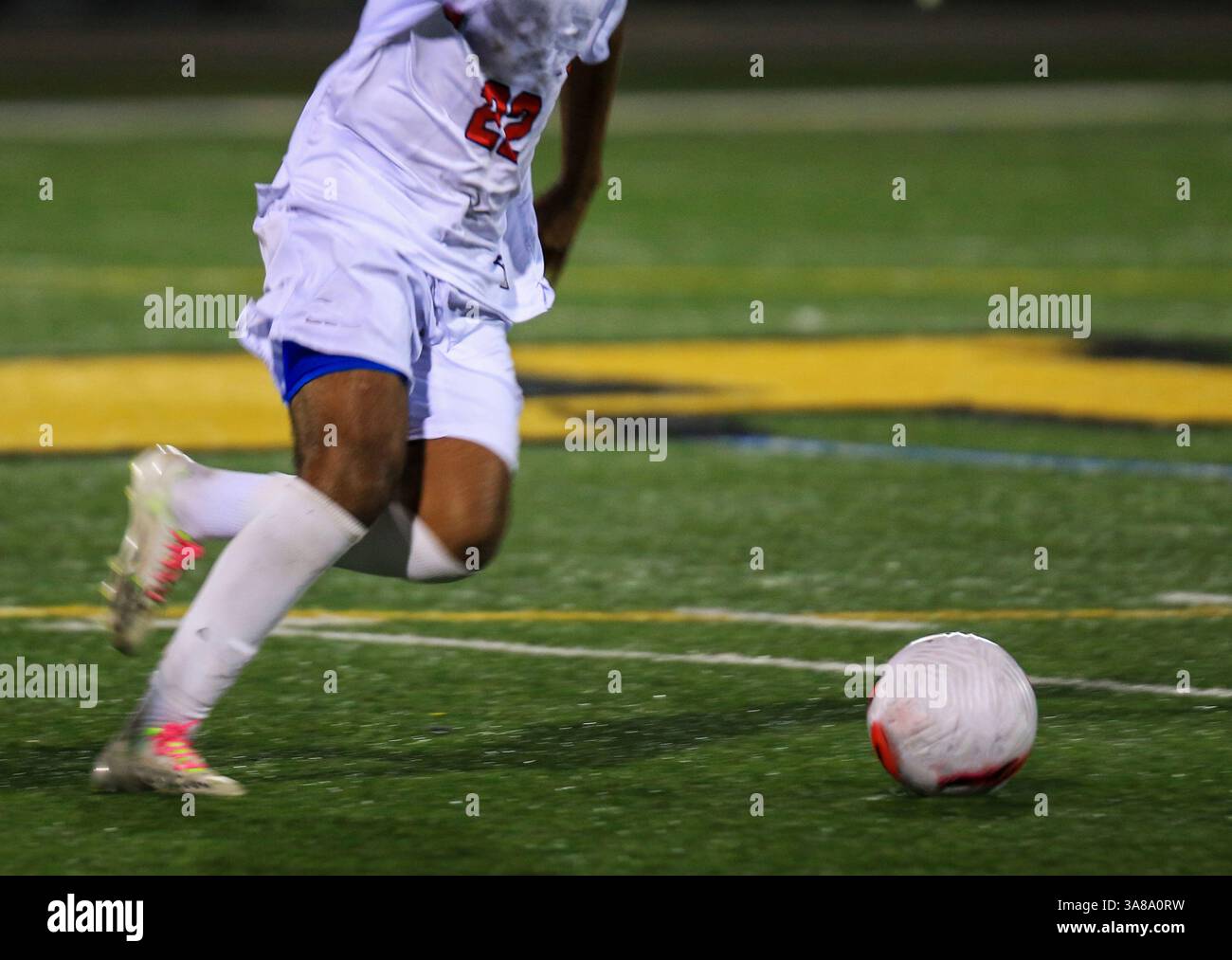 Atleta in uniforme bianca manovra abilmente una palla da calcio sul campo di erba di notte. Foto Stock