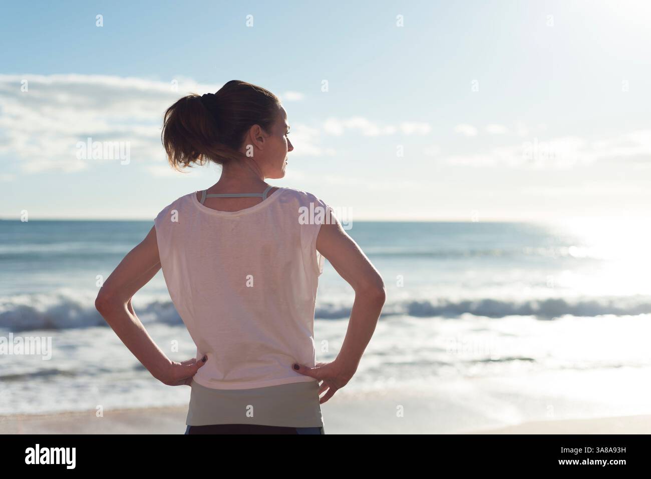 donna sportiva in piedi vicino all'oceano riposante dopo l'esercizio fisico, guardando verso il mare Foto Stock